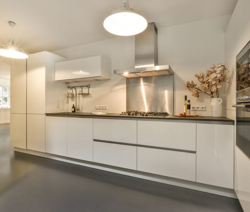 Modern minimalist style interior design of studio apartment with open white kitchen and dining zone with table and chairs illuminated by loft style lamp