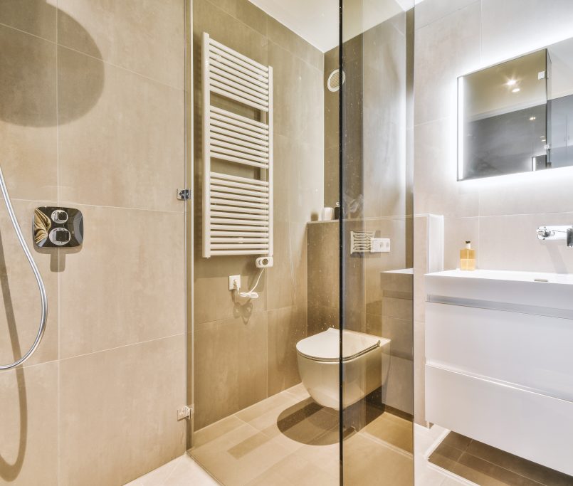 Modern flush toilet and ceramic sink installed on white tiled walls near mirror and towel in small restroom at home