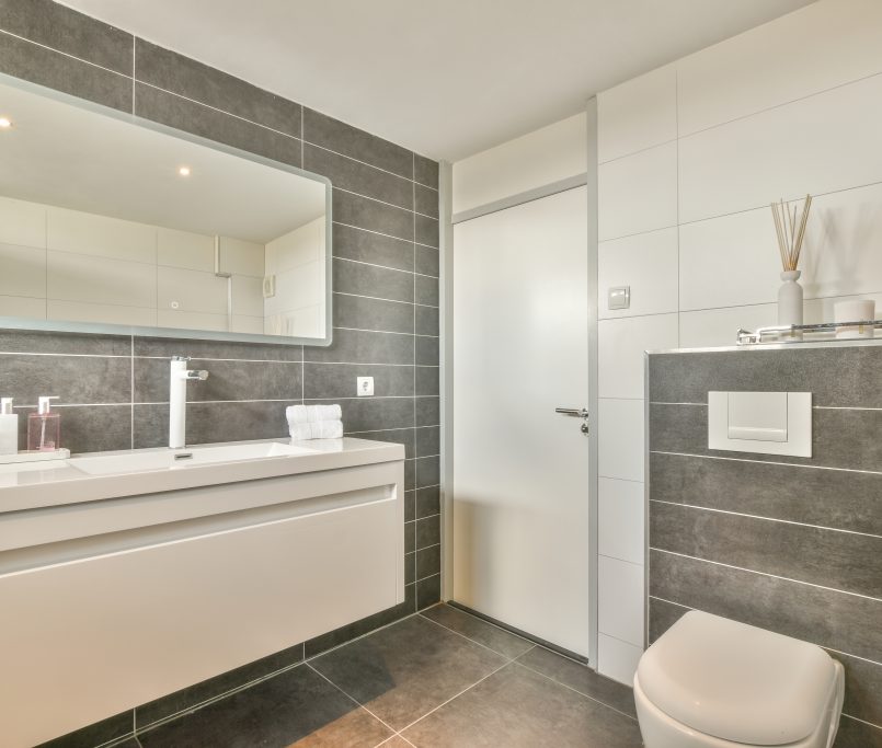 Modern flush toilet and ceramic sink installed on white tiled walls near mirror and towel in small restroom at home