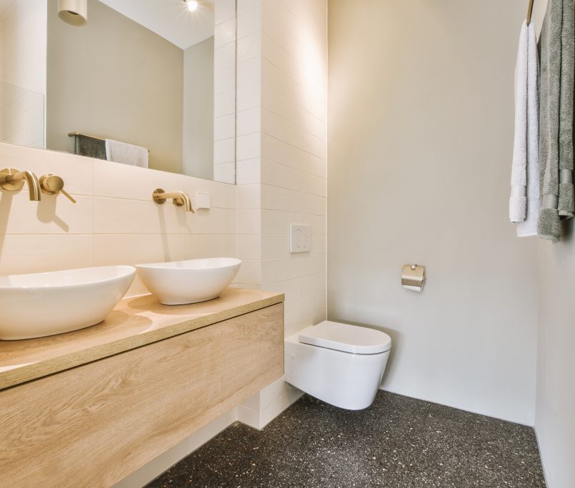 Modern flush toilet and ceramic sink installed on white tiled walls near mirror and towel in small restroom at home